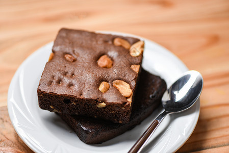 餐桌上的蛋糕巧克力蛋糕切片盘子里有坚果的巧克力蛋糕片木本底有勺子图片