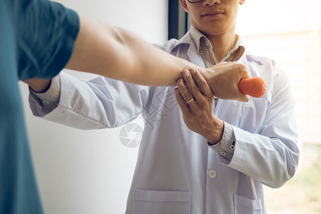 胸部按摩亚洲年轻男理疗师帮助病人在办公室里举起哑铃锻炼背景