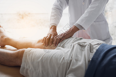 理疗师用手握着病人的大腿检查诊所疼痛和按摩情况背景图片