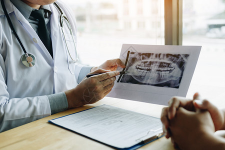 牙科医生手持笔指着X光照片与病人谈论药物和外科治疗图片