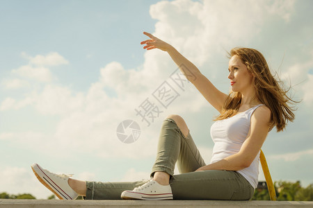 坐在水泥墙上的年轻时装模特儿身着白色顶和橄榄绿裤子图片