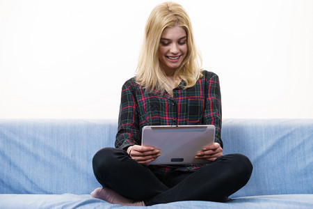 快乐的年轻少女在坐沙发上时使用平板在互联网上放松冲浪图片