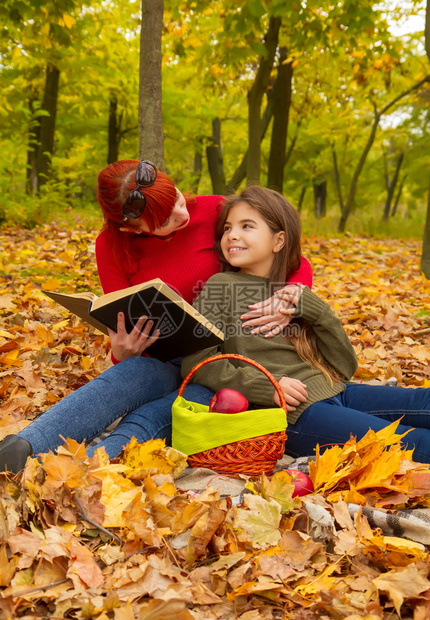 身穿明亮毛衣的年轻母亲和女儿在大自然野餐上一起阅读本书图片