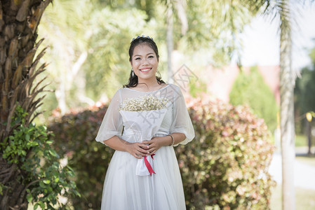 美丽的亚洲女新娘肖像在户外花园公中微笑并握着花束图片