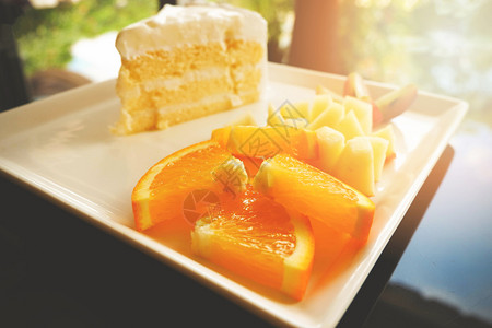 白盘上的切片水果和牛奶蛋糕关闭餐桌上有蛋糕奶油香草甜点的盘子上新鲜橙葡萄和苹果水切片图片