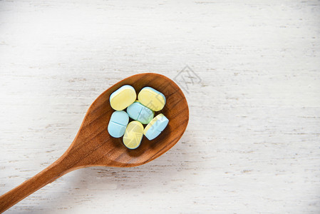 药片店白木桌面底的木勺中黄色和蓝的药片抗生素图片