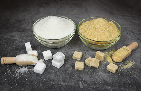 白糖和棕立方体以及碗上加糖和桌底木勺上加糖图片