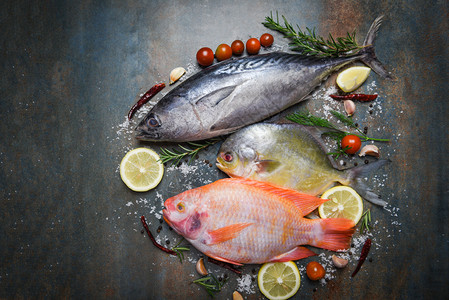 含有草药和香料的新鲜鱼迷迭香药和煮熟食品的柠檬大蒜番茄生鱼红罗拉番茄金鱼和黑板底的乌冻鱼图片