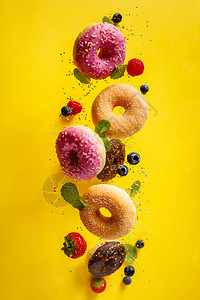 各种装饰的甜圈喷洒着糖和浆果在摇摆不定的背景中落下甜圈在摇摆或飞动中落下图片