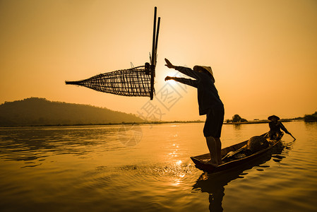 渔民在船上河日落亚洲渔民在木船日落或湄公河出木船落上捕竹鱼陷阱具有山地背景生命的Silhouette渔民船背景图片