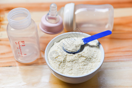 罐头勺里的奶粉和木桌背景上的婴儿奶瓶图片
