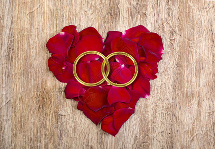 红花瓣的心和木桌上金婚戒指图片