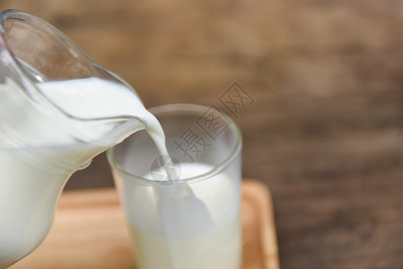 在玻璃壶里放天然新鲜牛奶在木制背景上将牛奶倒入玻璃图片