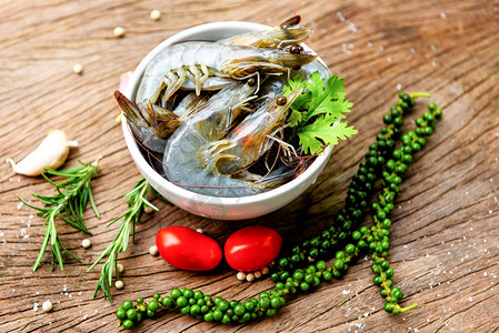 白碗新鲜虾和木制底配有食用海产品生虾的饲料草药和香背景图片