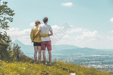 夫妇徒步旅行站在草地上享受远城风景图片