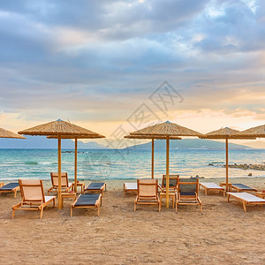 日落时海边有几排草伞的海滩图景图片
