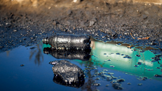 被石油和有毒废物污染的泥地上塑料瓶的胶片沾染着石油和有毒废物污染的泥地上塑料瓶的胶片对环境和生态危害的概念图片