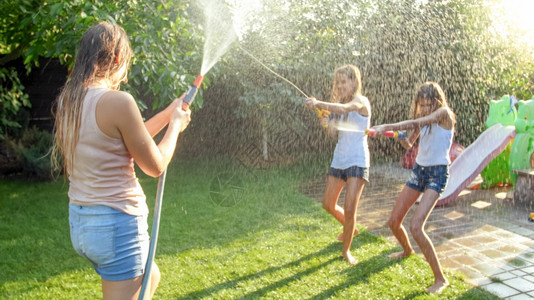 花园玩耍喜笑家庭与孩子们在热暑日玩得开心的美丽照片他们有水和花园龙头家庭在夏季玩耍和户外乐喜笑家庭与孩子们在热暑日玩得开心的美丽形象他们背景