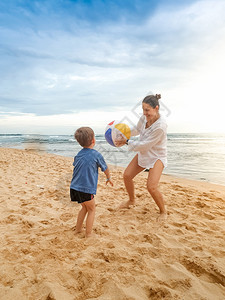 快乐的小男孩和年轻母亲在海滨玩沙滩球图片