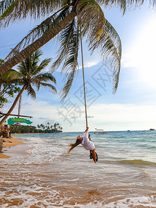 美丽的女士挥舞着绳子绑在海滨椰棕榈上美丽的年轻女士挥舞着绳子绑在海边椰棕榈上背景图片