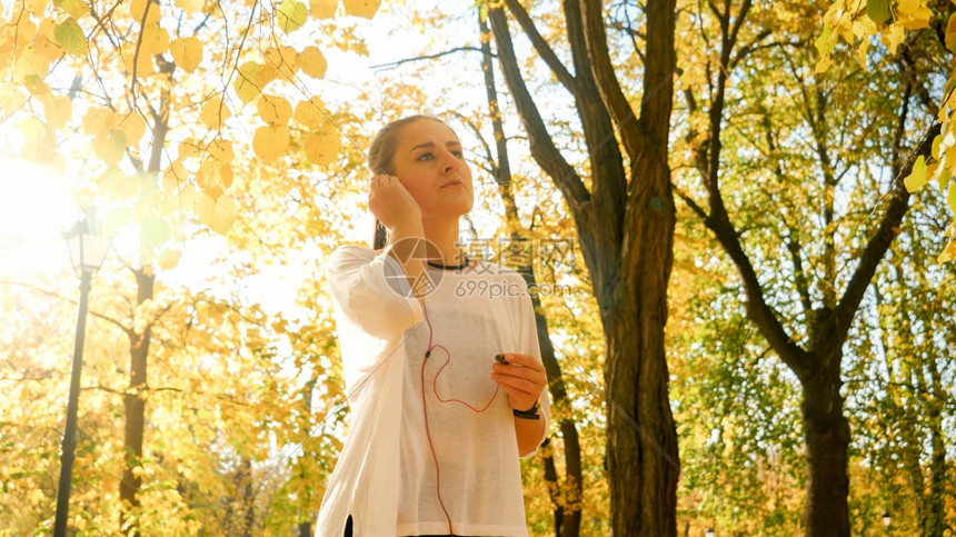 美丽的年轻女子在秋天公园慢跑前用耳机和音乐戴的肖像图片