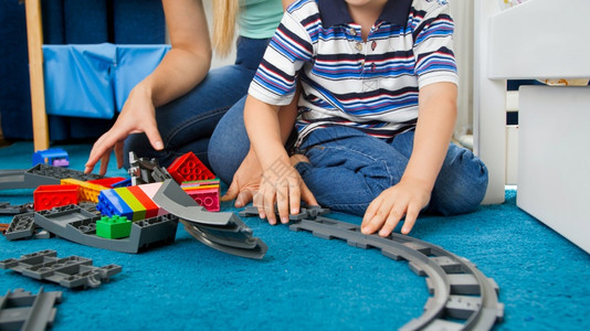 小孩男的近距离图像小孩的年轻母亲在地板上装配玩具铁路小孩男的近距离图像小孩的年轻母亲在地板上装配玩具铁路图片