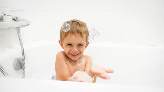 喜笑的男孩在洗澡时浴和手头上的香皂泡喜笑的男孩在洗澡时浴和手边的香皂泡图片