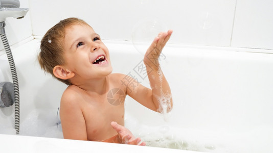 快乐的男孩在洗澡时玩肥皂泡和沫图片