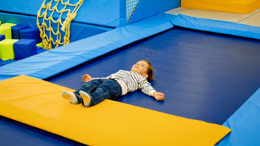 可爱的疲累小男孩在游乐场玩完和跳之后躺在蹦床上图片