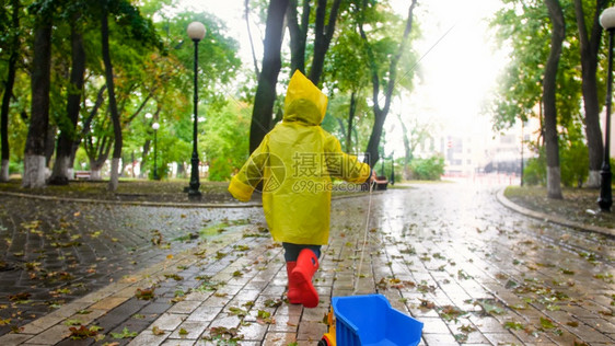 雨天在公园穿雨衣拿绳子拖玩具卡车的男孩图片