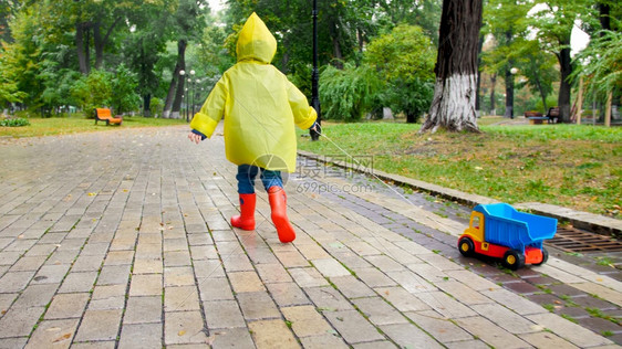 雨天在公园穿雨衣拿绳子拖玩具卡车的男孩图片