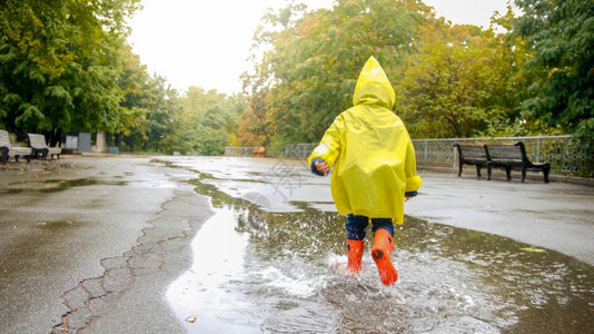 穿着橡皮靴的小男孩在公园雨后大水坑里跑来去图片