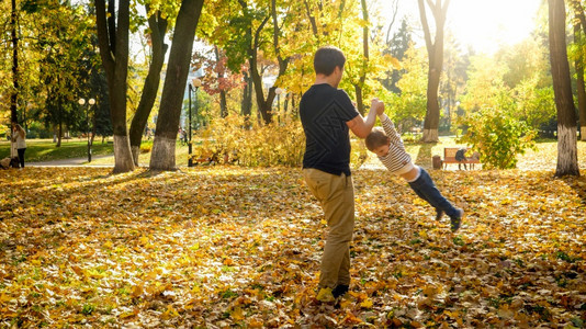 年轻父亲用手抱着儿子在秋天公园旋转图片