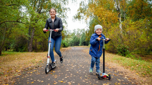 快乐的男孩和母亲一起在秋天公园踢脚踏车赛跑图片