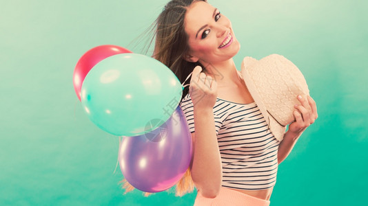 快乐和夏天年轻有魅力的快乐女人戴着草帽满身多彩的气球绿色背景玩彩气球的快乐女孩图片