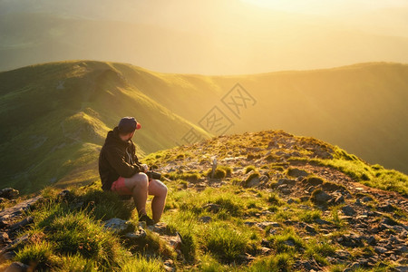 美丽的山雾中年轻男子坐在山顶的石头上夏天日落时风景与休闲男子一起漫步绿草阳光照亮的山丘旅行图片