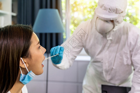 使用个人防护设备服的医务人员在家中用喉咙吸盘对亚洲妇女进行新冠coronaviruscovid19测试在家中提供新的正常保健服务图片