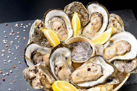 新鲜的牡蛎在黑石板上的篮子里塞柠檬新鲜的海食品和欧洲烹饪美食的概念图片