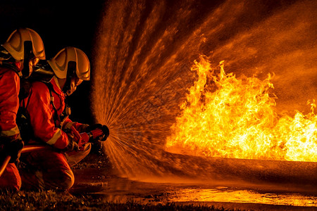 消防员使用Twirl水雾型灭火器与油的焰抗争以控制火势不扩散消防员和工业安全概念图片