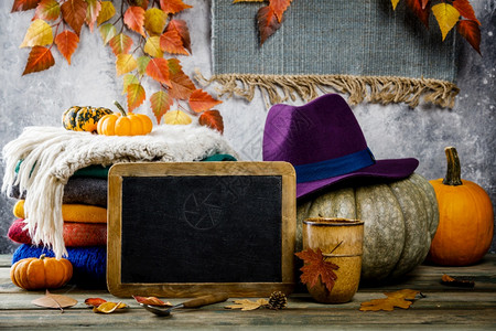 南瓜紫色的帽子编织衣服茶杯和木制小板上叶子的秋幕背景与南瓜茶叶和木制小板上叶子与古老的生锈长袍文字空间图片