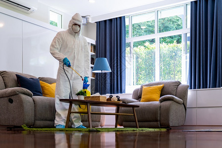 个人防护设备亚洲医务人员PPE防护服喷洒消毒雾剂在起居室喷洒科罗纳新冠19图片