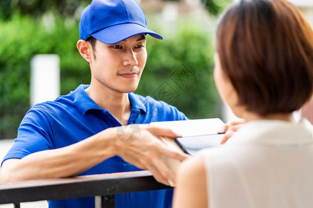 亚洲人向家庭前的亚洲女提供男子处理包箱女客户在便携式移动设备上签署电子名提供包件购物和数字标志概念图片