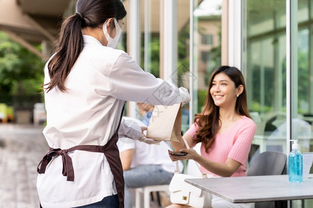 背面戴罩的亚洲女服务员背视向有吸引力的女顾客订购食品袋在冠状流行后在新的正常情况下取走或食品服务概念图片
