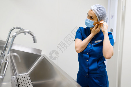 女外科医生在洗手盆附近戴面罩准备手术穿制服的医生门诊和保健人员女外科医生戴面罩准备手术女外科医生戴面罩准备做手术女外科医生戴面罩图片