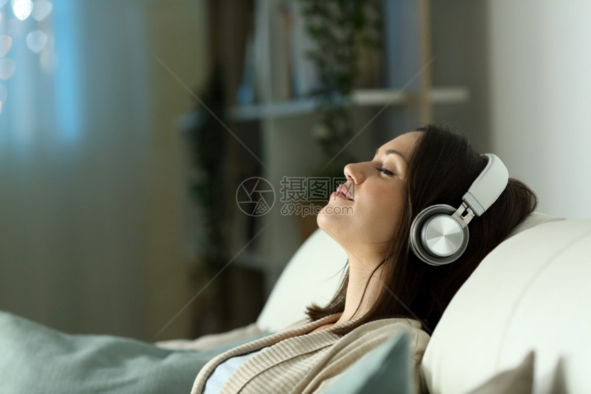 一位放松的女在晚上用耳机听音乐坐在家中客厅的沙发上