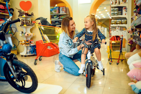 母亲和可爱的女儿在玩具店展览快乐童年家庭在商店购买自行车妈和小女孩在子的商店购买自行车妈和小女孩在子的商店购买自行车图片