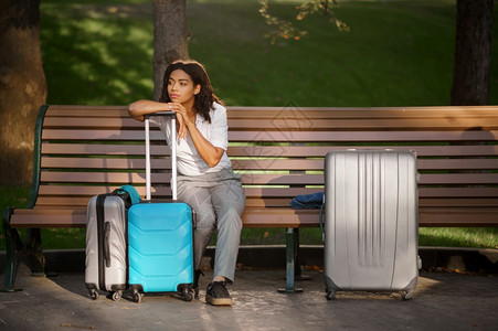 在夏季公园的长椅上坐着手提箱的年轻妇女在户外随身携带行李闲暇的女旅者在大自然中随身携带行李包的乘客在城市小巷上携带行李的女童在公图片