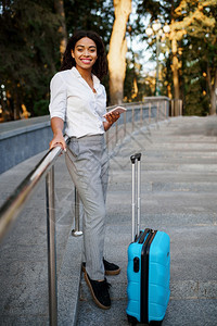 在夏季公园的楼梯上挂着手提箱的微笑妇女在户外随身携带行李闲置的女旅者在自然中随身携带行李包的乘客在城市小巷上带行李的少女在公园楼图片