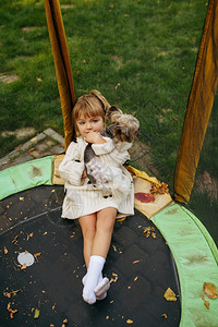 小孩在花园的蹦床上抱着狗狗图片