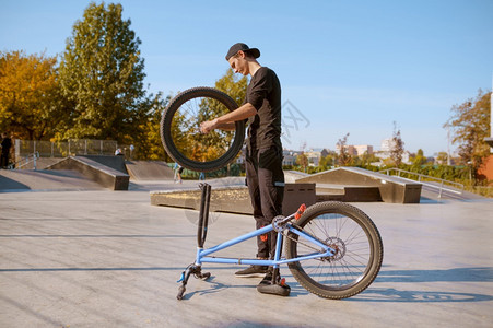 年轻的男bmx骑自行车者调整他的自行车在滑板场训练的青少年教极端的自行车运动危险的自行车运动危险的街头骑车在夏季公园骑自行车年轻图片